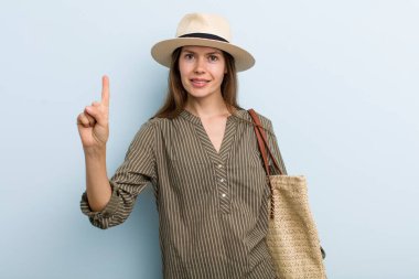 young adult woman smiling and looking friendly, showing number one. summer concept