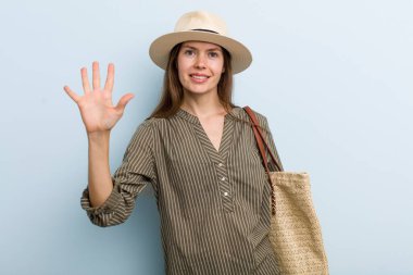 young adult woman smiling and looking friendly, showing number five. summer concept