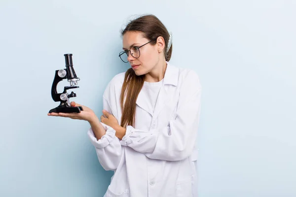 young adult woman shrugging, feeling confused and uncertain. scientist with a microscope
