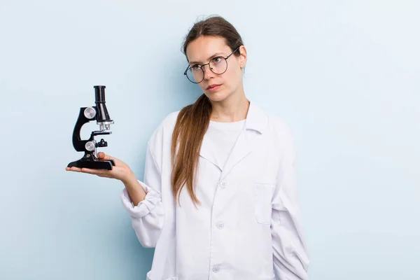 young adult woman feeling sad, upset or angry and looking to the side. scientist with a microscope