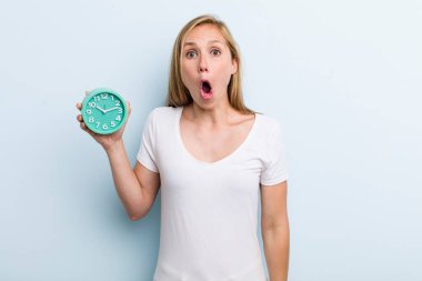 blonde young adult woman looking very shocked or surprised. alarm clock concept