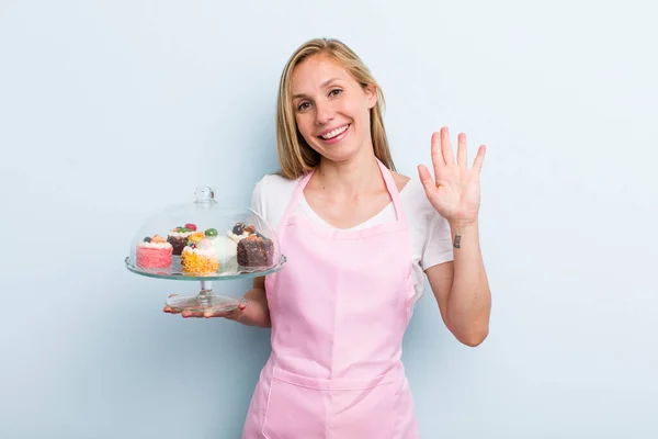 Blonde Young Adult Woman Smiling Happily Waving Hand Welcoming Greeting — ストック写真