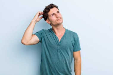 Genç yakışıklı adam şaşkın ve şaşkın hissediyor, başını kaşıyor ve yana bakıyor.