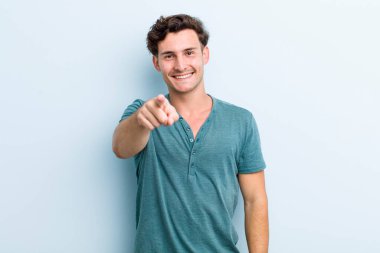 Genç ve yakışıklı bir adam kameraya bakıyor. Tatmin olmuş, kendine güvenen, dost canlısı bir gülümsemeyle seni seçiyor.