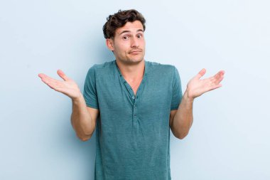 Genç yakışıklı adam şaşkın ve şaşkın, şüpheci, farklı seçenekleri tartıyor ya da komik bir ifadeyle seçiyor.