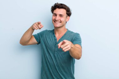 Genç yakışıklı adam mutlu ve kendinden emin, kamerayı iki eliyle gösteriyor ve gülüyor, seni seçiyor.