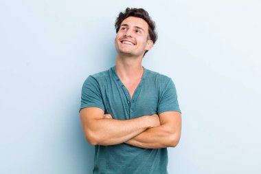Genç yakışıklı adam mutlu, gururlu ve umutlu, merak ediyor ya da düşünüyor, çapraz kollarla boşluğu dolduruyor.