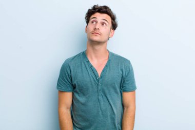 Endişeli, kafası karışık, budala bir ifadeyle genç yakışıklı adam, kopya alanı arıyor, şüphe ediyor.