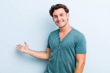 Genç yakışıklı adam kendini mutlu ve neşeli hissediyor, gülümsüyor ve seni selamlıyor, dostça bir jestle içeri davet ediyor.