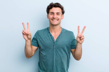 Genç yakışıklı adam gülümsüyor ve mutlu görünüyor, arkadaş canlısı ve memnun, işaret eden zafer ya da barış iki elle