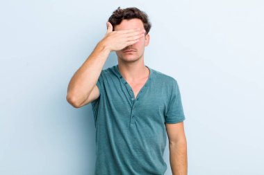 Genç yakışıklı bir adam tek eliyle gözlerini kapatıyor. Korkmuş ya da endişeli, merak ediyor ya da körü körüne bir sürpriz bekliyor.