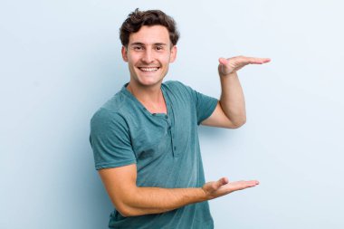 Genç yakışıklı adam gülümsüyor, mutlu, pozitif ve tatmin olmuş hissediyor, fotokopi alanında nesne ya da konsept tutuyor ya da gösteriyor