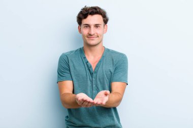 Genç yakışıklı adam mutlu bir şekilde gülümsüyor arkadaş canlısı, kendinden emin, olumlu bakışlı, bir nesne ya da konsept sunuyor ve gösteriyor.