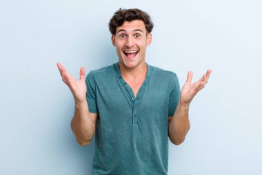 Genç yakışıklı adam mutlu, heyecanlı, şaşırmış ya da şok olmuş hissediyor, gülümsüyor ve hayrete düşüyor.