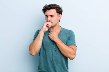 Gırtlağı ağrıyan, grip semptomları gösteren, ağzı kapalı öksüren genç yakışıklı bir adam.