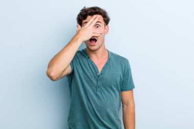 Genç yakışıklı adam şok olmuş, korkmuş ya da korkmuş görünüyor. Yüzü elle kaplanmış ve parmaklarının arasından gizlice bakıyor.