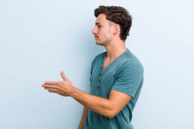 Genç yakışıklı adam gülümsüyor, seni selamlıyor ve başarılı bir anlaşma için el sıkışmayı teklif ediyor.