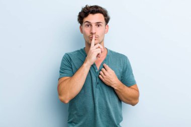 Genç ve yakışıklı adam ciddi görünüyor ve parmaklarını dudaklarına bastırıp sessizlik ya da sessizlik talep ediyor, sır saklıyor.