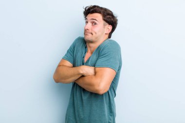 Genç yakışıklı adam omuz silkiyor, kafası karışık ve kararsız, kolları bağlı ve şaşkın görünüyor.