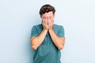 Genç yakışıklı adam üzgün, hayal kırıklığına uğramış, gergin ve depresif, iki eliyle yüzünü kaplayan, ağlayan