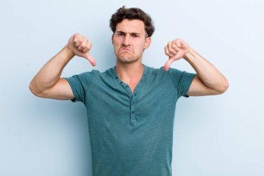 Genç yakışıklı adam üzgün, hayal kırıklığına uğramış ya da kızgın görünüyor, anlaşmazlık içinde baş parmağını gösteriyor, hayal kırıklığına uğramış hissediyor.