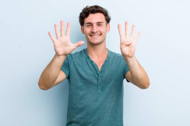 Genç yakışıklı adam gülümsüyor ve arkadaş canlısı görünüyor. 9 ya da 9 numarayı gösteriyor. Elleri önde, geriye doğru sayıyor.