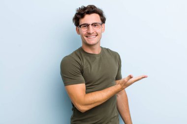 Genç yakışıklı adam neşeyle gülümsüyor, mutlu hissediyor ve fotokopi uzayında bir konsept gösteriyor.