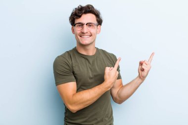 Genç yakışıklı adam mutlu bir şekilde gülümsüyor ve her iki elinde fotokopi alanında nesne gösteriyor.