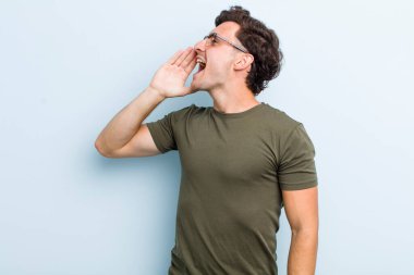 Genç yakışıklı profil görüntüsü, mutlu ve heyecanlı görünüyor, bağırıyor ve kenardaki boşluğu kopyalamak için arıyor