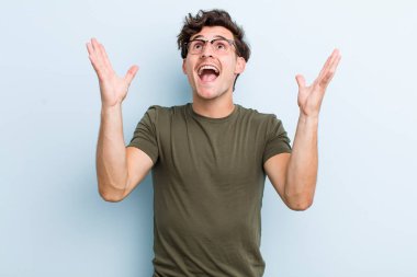 Genç yakışıklı adam kendini mutlu, şaşkın, şanslı ve şaşırmış hissediyor. Zaferi kutlarken iki elini de havaya kaldırıyor.