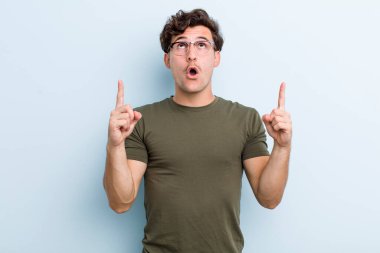Genç yakışıklı adam şaşırmış, şaşırmış ve ağzı açık, iki eliyle uzayı göstererek