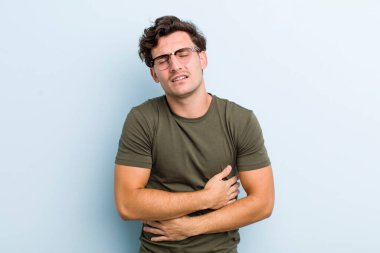 Genç ve yakışıklı bir adam endişeli, hasta, hasta ve mutsuz hissediyor. Ağrılı bir mide ağrısı ya da grip geçiriyor.