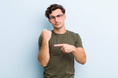 Genç yakışıklı adam sabırsız ve kızgın görünüyor, saati gösteriyor, dakiklik istiyor, zamanında gelmek istiyor.