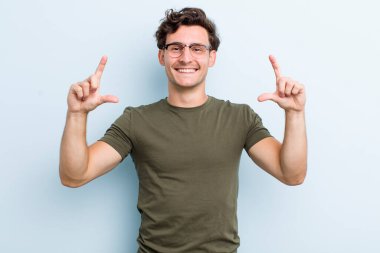 Genç yakışıklı bir adam kendi gülüşünü çiziyor ya da özetliyor iki eliyle, pozitif ve mutlu görünüyor, sağIık kavramı.