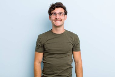 Genç yakışıklı adam mutlu ve şapşal görünüyor. Geniş, eğlenceli, kaçık bir gülüşü ve açık gözleri var.