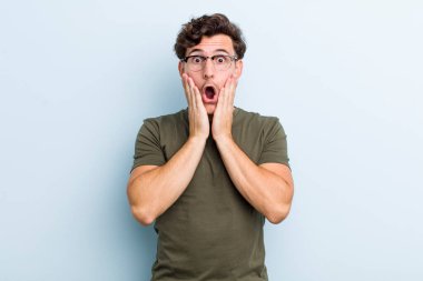 Genç yakışıklı adam şok olmuş ve korkmuş hissediyor, ağzı açık ve elleri yanaklarında korkmuş görünüyor.