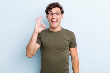 Genç yakışıklı adam kendini başarılı ve tatmin olmuş hissediyor, ağzı açık gülümsüyor, elle işaret veriyor.