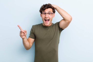 Genç yakışıklı adam gülüyor, mutlu, pozitif ve şaşırmış görünüyor. Yan fotokopi alanını işaret eden harika bir fikrin farkına varıyor.