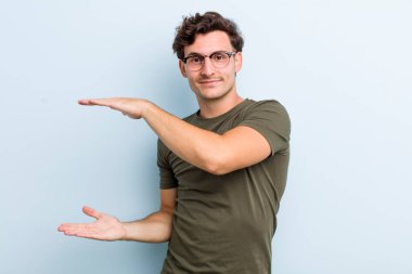 Genç yakışıklı bir adam iki eli de yan tarafında fotokopi alanı olan bir nesneyi tutuyor, bir nesneyi gösteriyor, sunuyor ya da reklamını yapıyor.