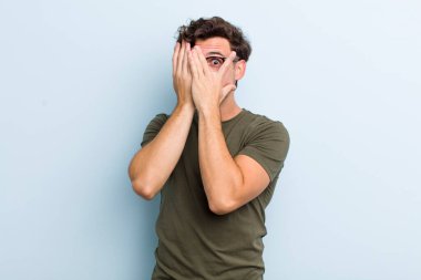 Genç ve yakışıklı bir adam korkmuş ya da utanmış hissediyor. Gözleri yarı kapalı ya da ellerle dikizliyor ya da dikizliyor.