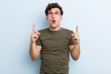 Genç ve yakışıklı bir adam şaşkınlık ve şaşkınlık dolu bakışlarla yukarıyı işaret ederek huşu içinde ve açık ağızlı hissediyor.