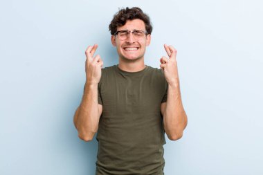 Genç yakışıklı adam gülümsüyor ve endişeyle iki parmağını çapraz yapıyor. Endişeli ve iyi şanslar diliyor.