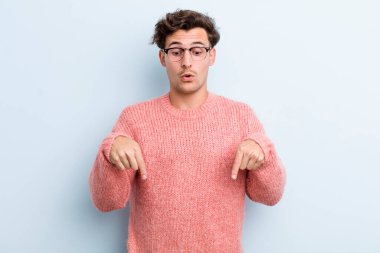 İki eliyle aşağıya bakan ağzı açık genç yakışıklı adam, şaşkın, şaşkın ve şaşırmış görünüyor.