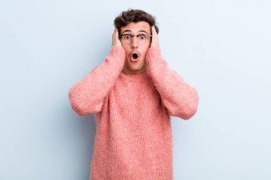 Genç ve yakışıklı bir adam hoş olmayan bir şekilde şok olmuş, korkmuş ya da endişeli görünüyor ağzı sonuna kadar açık ve iki kulağını da elleriyle kapatıyor.