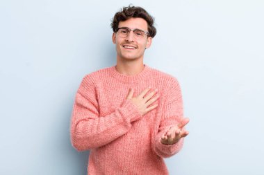 Genç yakışıklı adam mutlu ve aşık, bir eli kalbinin yanında, diğer eli önde uzanmış gülümsüyor.