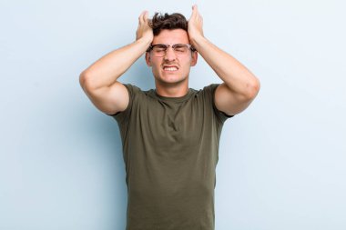 Genç ve yakışıklı bir adam stresli ve endişeli, depresyonda ve hayal kırıklığına uğramış, iki elini de başa kaldırıyor.