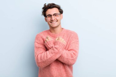 Genç yakışıklı adam, neşeli bir şekilde gülümsüyor ve kutluyor. Yumruklarını sıkmış, kollarını kavuşturmuş, mutlu ve pozitif hissediyor.