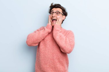 Genç yakışıklı adam mutlu, heyecanlı ve şaşırmış hissediyor, iki eli yüzü yana bakıyor.