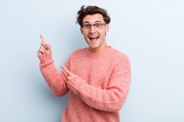 Genç, yakışıklı bir adam kendini neşeli ve şaşırmış hissediyor. Şok olmuş bir ifadeyle gülümsüyor ve bir tarafı işaret ediyor.