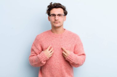 Genç ve yakışıklı bir adam kendini işaret ediyor. Şaşırmış ve şaşırmış bir şekilde bakıyor.